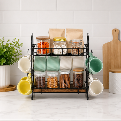 A black metal two-tier coffee mug rack with a wooden shelf base, styled on a white marble countertop with mugs, jars, and kitchen accessories against a white tiled wall. 2-Tier Coffee Bar Organizer with Mug Hooks. Vitly Hub