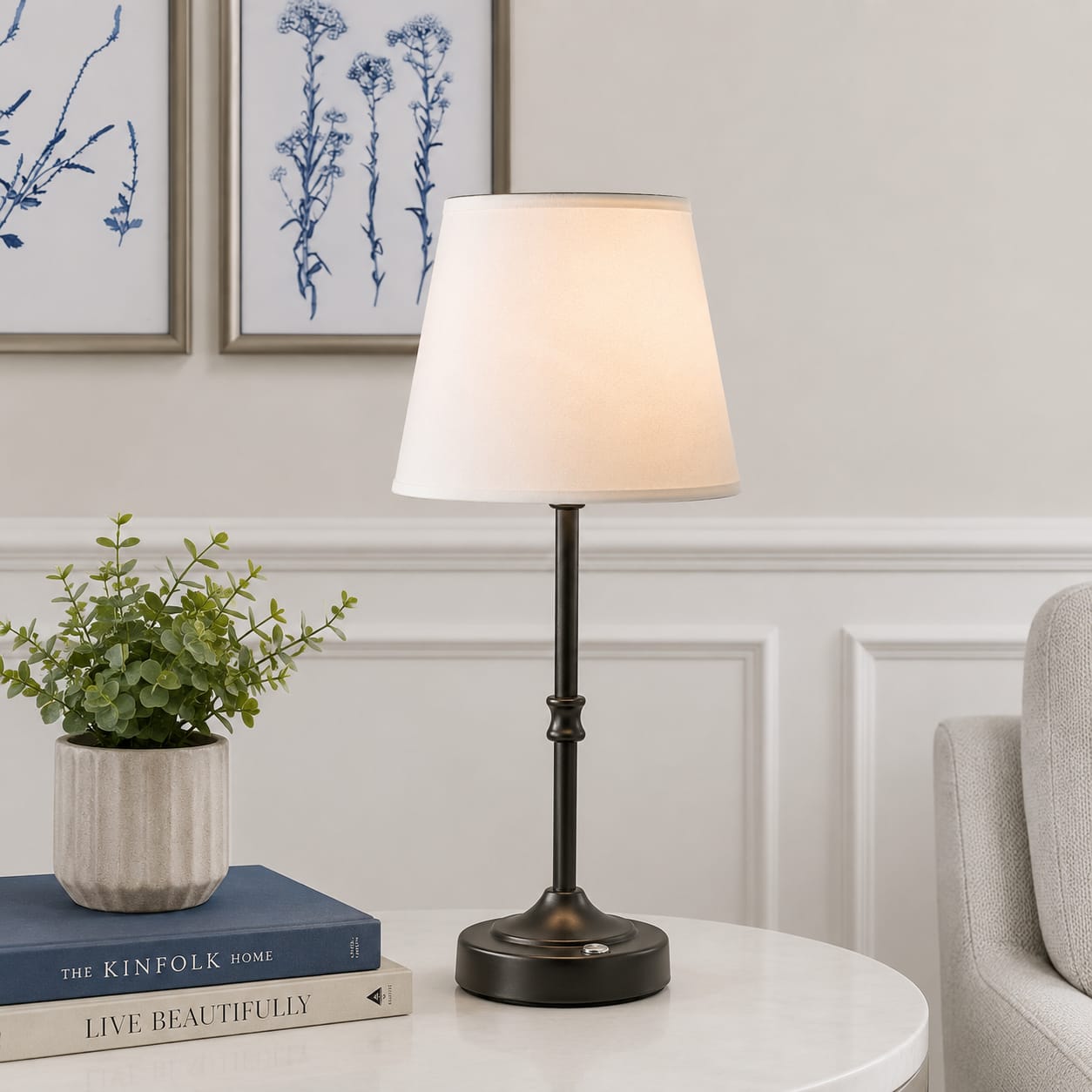 Table lamp on a round table with books and a plant in a living room setting.