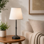 Table lamp on a side table next to a couch with a plant and framed picture in the background