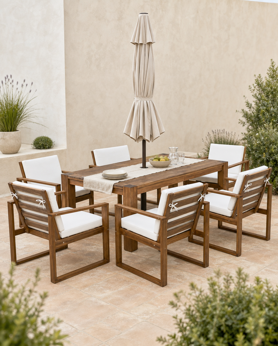 A 7-piece outdoor dining set featuring a rectangular wooden table, six matching armchairs with white cushions, and a closed beige patio umbrella, arranged on a stone patio against a stucco wall.