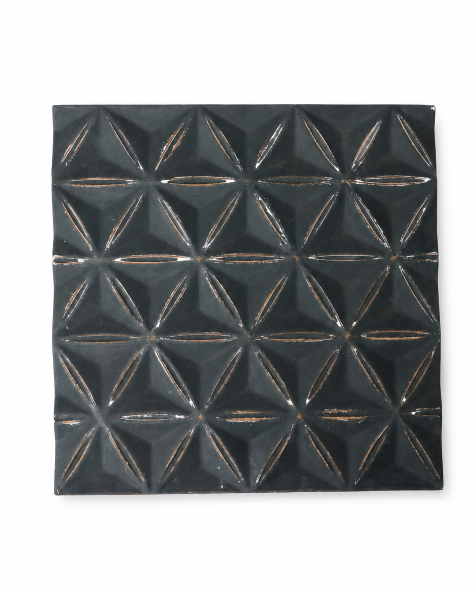 A square black textured wall tile with a raised geometric starburst pattern and distressed metallic bronze-gold lines, shown on a plain white background.