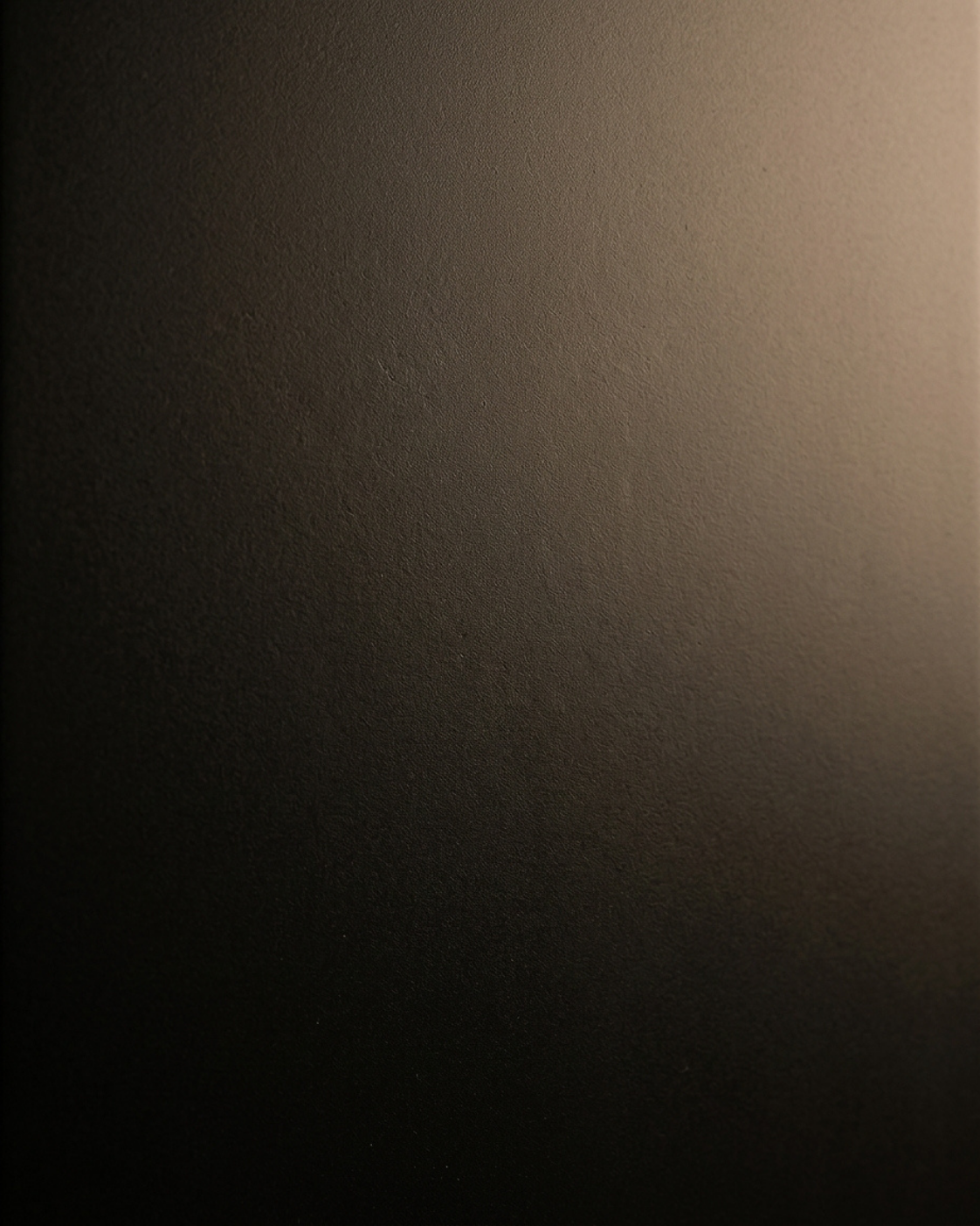 A close-up of a dark brown textured surface with a warm gradient of light shining from the upper right, highlighting the fine grain and matte finish.